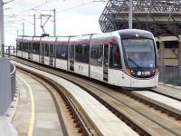 Edinburgh Tram 257 comes off the Roseburn Street bridge into Murrayfield tram stop on 4 August 2015. Haymarket Depot is off to the left and part of Murrayfield stadium can be seen on the right.<br><br>[Bill Roberton 04/08/2015]