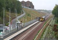 September 14th 2015 was a particularly dull Monday morning. Even by 0930, car headlights were being automatically activated and various shop windows were still illuminated along Main Street in Newtongrange. The station itself displays an overall grey pallor as the 0859 Tweedbank - Edinburgh approaches. In the background is the now completed zig-zag path linking the station car park and the National Mining Museum. This is the first time I can recall using the ISO 6400 setting on a camera.<br><br>[John Furnevel 14/09/2015]