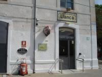 The platform side entrance to the ticket office at Llanca, on the section of line between Portbou and Figueres, with decoratively tiled station name above the door. A clock can be seen alongside the door, with a small RENFE plate and the evacuation plan for that location below. There is also a descriptive oval plate, showing a measurement as at Portbou, mounted above the fire extinguisher.      <br><br>[David Pesterfield 07/08/2015]