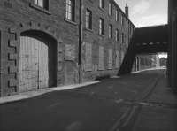 The Westburn Iron Foundry, Arbroath, was established on either side of Orchard Street in buildings formerly marked as Westburn Works (Flax, hemp & co) on the 1859 OS map. This photograph shows a railway track linking two of the buildings which appears on the 1921 and later OS maps. This track is presumed to have been manually worked, linking two buildings under the same ownership, and there is no evidence of the tracks extending beyond the works. Douglas Fraser and Sons Ltd owned a number of mills in Arbroath.<br><br>[Bill Roberton //1987]