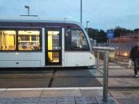 The cab end of an airport-bound tram at Murrayfield at dusk on 06/10/2015. An alighting passenger crosses the tracks in front of the tram. the first time I visited this elevated station I wondered where the subway could be! Notice the fuel tanks of Scotrail's Haymarket depot in the background. Haymarket is a bit of a misnomer, though the depot was originally further east.<br><br>[David Panton 06/10/2015]