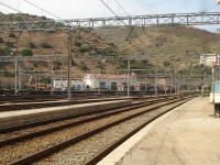 Adif liveried centre cab Bo-Bo diesel shunter 311.126 makes a very speedy exit from the yard at Portbou, making for the tunnel into France en route to Cerbere yard, with a lengthy rake of intermodal container flat wagons [See image 52756]<br><br>[David Pesterfield 07/08/2015]