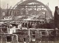 The original 1876 arched roof of St Enoch seen under construction from the west showing the undercroft. The second roof was added in 1901 and built to the south (right) of the original and the approach lines quadrupled through to Port Eglinton Junction. With the two routes to Paisley and the Lochwinnoch Loop this quadrupling effectively continued through to Dalry Junction. The small roofs seen beyond the station are those of Dunlop Street, the terminus of the line from 1870 until the large station was completed.<br><br>[Ewan Crawford Collection //]