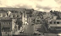 The entrance to the original Fort William station at Station Square seen in a postcard view, probably from a vessel at the MacBrayne's Pier. That's almost certainly a connecting bus at bottom right. The station building to the left and modern building to the right were both swept away when the railway was cut back and a dual carriageway built along the seafront. The Station Hotel (now the Highland Hotel) stands above all on the hill.<br><br>[Ewan Crawford Collection //]