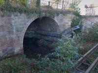 Just to the north of the ECML, and just shy of Baileyfield S and C Works, stands this original Edinburgh and Dalkeith Railway bridge. This view looks west from Sir Harry Lauder Road at the bridge over the Figgate Burn on their Leith branch. The bend in the conduit shows where the later (1858) NBR line bridge was built alongside which gave the NBR access to Leith from Portobello and paved the way for the closure of the Portobello-Niddrie section.<br><br>[Bill Roberton 24/11/2015]