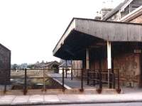 Looking north east across Bridge Street, Kirkcudbright, on 22 September 1970. By this time the former terminus had been closed for over 5 years, although the station 'Gents' on the right remained in public service. In the distance are the abandoned locomotive shed and signal box, while the wall of the old goods shed stands on the left. Not long afterwards much of the area was cleared to make way for a housing development, although the station buildings themselves survive in other guises – even the Gents! [See image 25445] <br><br>[John Furnevel 22/09/1970]