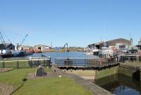 The still active Glasson Dock, seen from the swing bridge above the Lancaster Canal Basin lock in March 2016. The tracks of the Glasson branch continued beyond the station down the right hand quay and also behind the buildings on the right. On the left of the picture the blue vessel being loaded is the MV <I>Silver River</I>, which operates a daily general cargo service between Glasson and Ramsey in the Isle of Man. <br><br>[Mark Bartlett 07/03/2016]