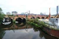 A Manchester Airport to Blackpool service with a pair of Class 156 DMUs crosses the River Irwell on the approach to Ordsall Jct in the afternoon of 4 June 2016. On the right is one of the worksites for the new Ordsall curve although the curve will be on the other side of the viaduct. Looking along the river beyond the first viaduct is an arch of the original L&M viaduct. Beyond that is the reflection of the Princes St girder bridge.<br><br>[John McIntyre 04/06/2016]