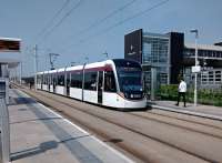 A city-bound tram pulls into the stop on a very warm 07/06/2016 with the network station in the background, with its revolving footbridge (if only). The name of the stop is I suppose inevitable, even if most of the custom is for Hermiston Gait Retail Park (in literally 6ft high letters) on the other side of the road.<br><br>[David Panton 07/06/2016]