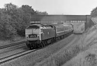 47 047 powers under the bridge carrying the Heath Common to Snydale road over the former MR main line just north of Oakenshaw North Junction. The wide spacing of the up and down lines betrays the fact that four tracks once existed here, but at least in 1975 the line was still carrying class 1 trains - indeed NE to SW expresses not calling at Wakefield had only recently reverted to this route as it was by then no longer plagued by colliery subsidence as had been the case in earlier years. Forty years later, no railway exists here and I presume the trackbed is occupied by a birch forest. The train is the 09:16 Leeds - London St. Pancras and the date is 2 August 1975<br><br>[Bill Jamieson 02/08/1975]