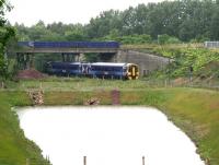 The 0911 Edinburgh - Tweedbank passes below Whitehill Road bridge in heavy rain, shortly after restarting the 0911 Edinburgh - Tweedbank from Newcraighall station on 12 June 2016. ScotRail 158871 is about to run past the Biogen attenuation pool before entering the double track section at Newcraighall South Junction.<br><br>[John Furnevel 12/06/2016]