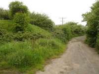 Looking north along a now blocked and by-passed section of the A174 coast road where a rail overbridge crossed the road around midway between Hinderwell and Staithes stations. The now chamfered off end of the embankment running from Hinderwell [see image 55506] can be seen ending to the left of the road, with the new section of the A174 now crossing the former trackbed on the level beyond the trees on the right.<br><br>[David Pesterfield 29/05/2016]