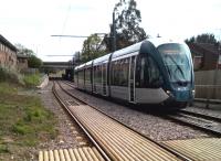 This tram is returning from the Clifton South terminus to Nottingham city centre. It has just curved onto the very straight [see image 10962] GCR trackbed, which went straight ahead South through the vegetation visible under the distant road bridge.<br><br>[Ken Strachan 23/04/2016]