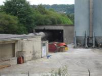 Looking across the former L&Y main line to the Hope Construction cement plant, with the off-loading of full tank wagons taking place in the background. Whilst there are two tracks through the building to allow two rakes to be off-loaded together, only the rake on the far line is being emptied one tank at the time. The second rake is stabled beyond the building and will eventually be pushed back and then drawn forward as unloading takes place. [See image 55995]<br><br>[David Pesterfield 22/07/2016]