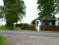 The Peebles Railway crossed the B7026 Auchendinny – Leadburn road at Loanstone, just under half a mile from Pomathorn station. On the east side of the crossing (behind camera) were two agricultural sidings. View is south west over the site of the level crossing towards Pomathorn on 2 August 2016, with a garage now occupying the trackbed. The fence on the right is supported by one of the original gateposts and beyond that is the former crossing box, standing in front of the refurbished gatekeeper's cottage. The Pentland Hills can just be seen in the centre background. The line closed completely in 1962.<br><br>[John Furnevel 02/08/2016]