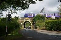 A Liverpool to Preston EMU on the down slow line passes over Pack Saddle Bridge on the A49 road (between Preston and Wigan) as road traffic heads south under the control of the traffic lights. While the original bridge supports two tracks (the slow lines) of the WCML, a newer bridge on the other side is now carrying three tracks, the fast lines and the up Chorley line.<br><br>[John McIntyre 09/08/2016]