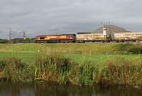 The thrice weekly Clitheroe to Mossend cement tanks will run via the WCML throughout 2016. 66099 powers north alongside the Lancaster Canal between Brock and Garstang & Catterall on the evening of 12th August 2016. The dome behind the tanks is the salt store of the Highways Agency depot for the nearby M6 motorway.<br><br>[Mark Bartlett 12/08/2016]