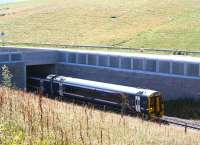 Northbound Scotrail 158735 emerges from under the A7 at the south end of Falahill village on 17 August 2016. The train is the 1259 Tweedbank - Edinburgh. The road runs immediately beyond the wall - note the extremely acute angle between road and railway, resulting in the lengthy 'diveunder' required here. <br><br>[John Furnevel 17/08/2016]