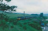 Large logo 'Highland Rail' Class 47 hauled Scotrail (BR) coaching stock on its way to Aberdeen with a stop at the recently re-opened Dyce Station. Shot is taken from the Old Dyce Kirk overbridge looking northeast. In contrast to the view to the south west [see image 57712] very little has changed here-only the telegraph poles have gone.<br><br>[Charlie Niven /07/1988]