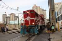 Loco No 1505 of the New Orleans Public Belt Railroad brings a freight train along the Mississippi riverfront across one of the many open crossings along the riverfront. On the right of the crossing is the Riverfront Shopping Mall and the Cruise Ship Terminal.<br><br>[Alastair McLellan 09/11/2016]