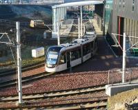 A city bound tram pulls away from the platform at Edinburgh Gateway in bright late morning sunshine on 26 January 2017 and turns sharp right to pass below the A8 (top left). The tracks in the foreground run to the tram depot. Edinburgh Gateway Interchange was officially opened on 11 December 2016.<br><br>[John Furnevel 26/01/2017]