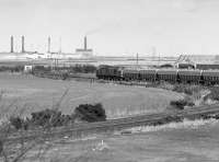 A class 37 heading for Lynemouth smelter (closed in 2012) approaching Hirst Lane Level Crossing. In the foreground is the former west to east curve at Ashington which allowed direct running from Ashington Colliery to Lynemouth. The smelter and power station are in the background.<br><br>[Bill Roberton //1987]