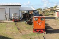 Locomotives at Needsmust Depot, St Kitts. No.15 has been renovated and is used for occasional maintenance trains. Two stablemates from sugar cane days lurk in the right hand shed while one of the Romanian built hydraulics is undergoing a repaint. The modern building behind is the terminal of the airport.<br><br>[Mark Bartlett 18/02/2017]