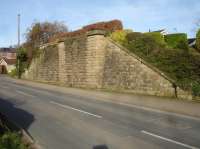 A large retaining wall, incorporating the abutment for a single track rail over-bridge, is still extant on the east side of Clint Bank, at the west end of the former Pateley Bridge branch station at Birstwith.  The view is looking north east, with houses built on the former goods yard visible to the right beyond the remaining section of embankment alongside the station site. <br><br>[David Pesterfield 26/03/2017]