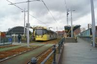 A Metrolink tram calls at Deansgate-Castlefield whilst working to Manchester Airport on 19 May 2017. Deansgate railway station is to the right and the roof of the former Manchester Central station is in the left background.<br><br>[John McIntyre 19/05/2017]