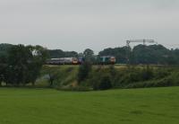 A southbound Pendolino hides most of a long <I>Tesco train</I> heading north at Bay Horse behind nearly new DRS electro-diesel 88005 <I>Minerva</I> on 25th July 2017. <br><br>[Mark Bartlett 25/07/2017]