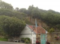 A view looking up to the former Sandsend Station building from the road at the bottom of the A174 Lythe Bank showing the height of the trackbed above the road immediately south of the station, and needing a substantial bridge to cross both the road and the nearby Sandsend Beck to continue on to Whitby West Cliff Station. <br><br>[David Pesterfield 06/08/2017]