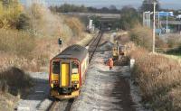A Carlisle bound DMU slows for the stop at Gretna Green on 6 November 2007. In the right foreground is part of the workforce engaged on the Annan - Gretna re-doubling project. Meantime, a northbound service is held at signals below the bridge in the background awaiting access to the single line section. <br><br>[John Furnevel 06/11/2007]