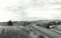 A view south over the site of the never opened Lyoncross station on 8 September 1960, with BR Standard tank 80107 passing on a Neilston High - Glasgow Central train. The junction was beyond the train on the other side of Aurs Road.<br><br>[G H Robin collection by courtesy of the Mitchell Library, Glasgow 08/09/1960]