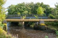 This bridge crosses the Garnock and carried the substantial Doura branch of the Ardrossan and Johnstone Railway. The view looks south. Eglinton Iron Works was to the right and Dirrans station was to the left. The closer pipe bridge is not related. A second bridge was beyond, this carried the mineral line to Eglinton Colliery No 1 Pit and Bogside Coal Pit No 1.<br><br>[Ewan Crawford 14/09/2017]