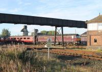 Framed by the old shed access footbridge, WCRC 57601 slowly propels a rake of MkII stock towards the Carnforth Down Goods Loops prior to departing for Norwich with an ECS working on 22nd September 2017. The signal box is Carnforth Station Junction and the lines in the immediate foreground are for Settle Junction via Wennington. <br><br>[Mark Bartlett 22/09/2017]