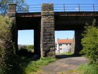 From Glengarnock Ironworks a line headed west to serve ironstone pits and also south to serve coal mines in the Dalry area. From the ironworks the line descended to and then crossed the B777. After crossing the river Garnock, where the abutments still serve to support a footbridge,  it headed due west along what is now Balgray Road and on into Loadingbank. It pre-dated construction of the G&SWR Lochwinnoch loop line so when the G&SWR line was built it crossed the line by this bridge which as can be seen accommodated the mineral railway on the left side and the road on the right. View looks west towards Loadingbank.<br><br>[Douglas Blades 05/05/2017]