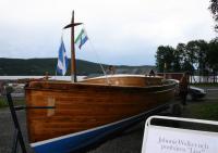 This former Post Boat was last seen at Huså on the shores of Kallsjön in Jämtland northern Sweden. The sign on the right has some text explaining how she got there. I offer a translation of the sign without further comment. Viewers can decide for themselves: 'Lisa was built in Dublin at the end of the 19th Century. She arrived by train at Järpen Station accompanied by an English sea captain who brought her across Kallsjön Lake to Sundet. She was transported onwards to Lake Anjan using the aerial ropeway belonging to Verdal Bruk; 'Johnnie Walker' had a hunting lodge on the western side of the lake. She was used mainly to transport hunting guests to the grouse moors on the east side of Lake Anjan. Eventually Berhard Mona from Fäviken received her in exchange for the grouse shooting rights in that area. During her time on Kallsjön she was used, amongst other things, as a Post Boat. The boat was found under a tarpaulin in Björnänge by the Friends of Lisa Society' (Lisas Vänner).<br>
As the sign contains some artwork representing someone looking like JW of whisky fame it would probably be in breach of copyright to show it. Note the Saltire and the flag of the 'Republic of Jämtland' on the forestay.<br><br>[Charlie Niven 29/07/2009]