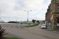 Looking south east over the site of the C&MLR station on Campbeltown quayside in October 2017. From 1906 to 1934 there were two lines of a run round loop laid in the road approximately where the flower bed now lies and the track terminated around the end of the building line. The logs on the pier in the background are awaiting shipping across the Firth of Clyde to Irvine. <br><br>[Mark Bartlett 31/10/2017]