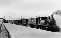 Judging by the pristine condition of the platforms, locomotive and carriages this image of Knott End station was taken around the time of opening in 1908. It was also taken before the glass <I>conservatory style</I> waiting area was attached to the building [See image 60609]. The locomotive is 0-6-0T <I>Knott End</I>, built by Manning Wardle for the opening of this extension to the line from Pilling. The open veranda carriages were built at the Lancaster Carriage and Wagon Works and were later used on the Wanlockhead branch in Scotland. Since closure the station has been completely rebuilt but the extension with the circular vent, visible here on the left, is still in use.  <br><br>[Knott End Collection //1908]