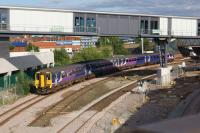 A Northern service from Blackpool to Manchester Airport passes under the new covered walkway between the railway station (right) and the new bus interchange (left) at Bolton on 09 August 2017. The remains of the long trailing crossover can be seen between the running lines and the track for the new platform 5 is on the extreme right.<br><br>[John McIntyre 09/08/2017]