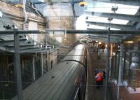 The Waverley 'sub' island platforms (8 & 9) seen looking east through a glass panel from the station walkway on 21 December 2017. Standing at platform 9 (W) is ScotRail EMU 334025 awaiting its departure time with the 1107 to Milngavie. The covered stairway on the left, built onto the station's south wall, was constructed in 2006 to provide access to the new through platform 10, which runs along the other side of the wall [see image 13170]. Note how the line and platform are forced to curve round the massive pier supporting the city's North Bridge, thus providing the space required to construct the new stairway and lift.    <br><br>[John Furnevel 21/12/2017]