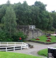 Scene at Summerlee Heritage Museum in August 2006 looking south east from the roadway alongside the main exhibition hall. On the left is the truncated southern end of the Gartsherrie Cut of the Monklands Canal, with a picnic area now occupying the area to the right. In the background is the fenced off north eastern abutment of the bridge that once brought the link from the M&K route over the canal and into the sidings at the south end of Summerlee Ironworks off to the right.   <br><br>[John Furnevel 29/08/2006]