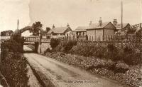 A postcard view of Friockheim viewed from the south. The rather curious appearance of the top left corner is due to an overly keen philatelist who tore the corner off for the stamp. The image is patched from another copy, but I thought I would leave the damage obvious. The station building is long gone, but the station house and east abutment of the bridge remain in place. The west abutment was swept away in road widening works.<br><br>[Ewan Crawford Collection //]