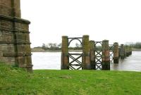 Remains of Alloa swing bridge seen from the north side of the Forth in 2006, showing the rail-banded northern abutment and surviving piers. Opened in 1885, the 21 span, wrought iron structure carried a single line 1,615 across the river linking Throsk and Alloa. The bridge incorporated a rotating span to permit passage of shipping, with a combined control cabin and signal box mounted above the rails . (The shorter piers –  the fifth set out from the north shore – supported the mechanism used to rotate the opening span). Passenger services ceased in 1968, while the last freight to use the bridge brought a final consignment of coal for the steam driven turning mechanism in May 1970. Dismantling took place during 1971.  <br><br>[John Furnevel 27/04/2006]