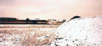 A southbound Intercity 125 has just passed below the A8 overbridge approaching South Gyle Station in December 1991. In the foreground is the site of the car park for the new Gyle Centre, still a green field except for a specially-engineered trial embankment of red blaes (covered in snow). In the background is the Royal Scot Hotel now the site of a retail store. [Ref query 4 April 2018]<br><br>[Charlie Niven /12/1991]