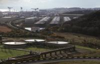 Looking west to Rosyth Dockyard in May 1989. The branch line curves in to the left, this being a later, direct route over reclaimed land.  The previous route curved to the right of the box-shaped building and past the fuel tanks, and was partially retained as a siding controlled from Limpetness frame. <br>
<br>
<br><br>[Bill Roberton /05/1989]