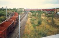 Looking north at the former Whifflet stations. On the left under the bridge was Whifflet Lower (Caley), above it was Whifflet Upper (Caley) and on the right was Whifflet (NB) which was an island platform accessed from the Caley Upper station. Iron Ore from Hunterston to Ravenscraig runs past on the left. At the time Whifflet (New) had not yet opened as the R&C line was chiefly used for freight and diversions.<br><br>[Ewan Crawford //1987]